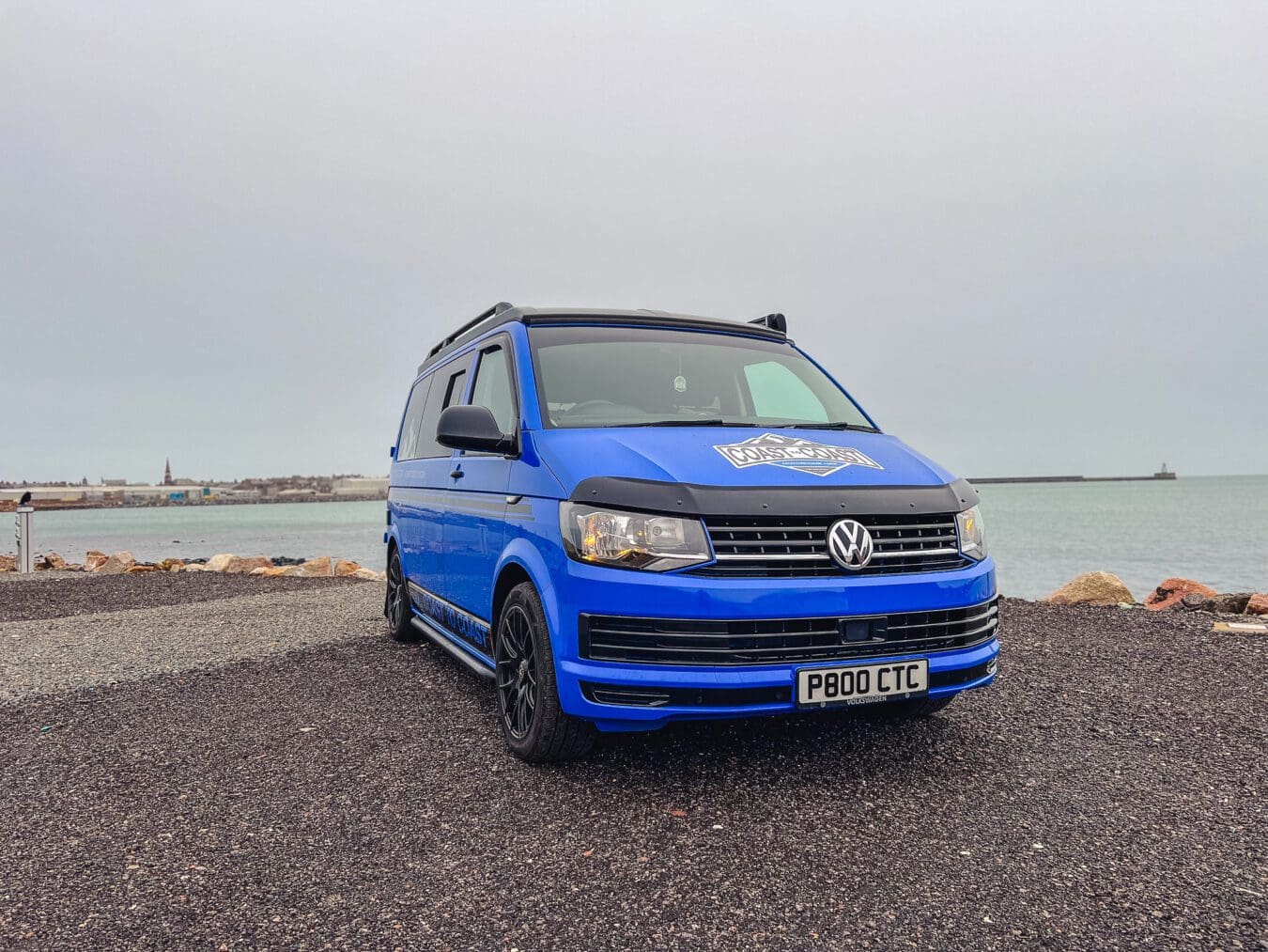 Home 22 Blue VW T6 Coast to Coast campervan with branding, parked by the coast near Peterhead, Scotland – available for campervan hire