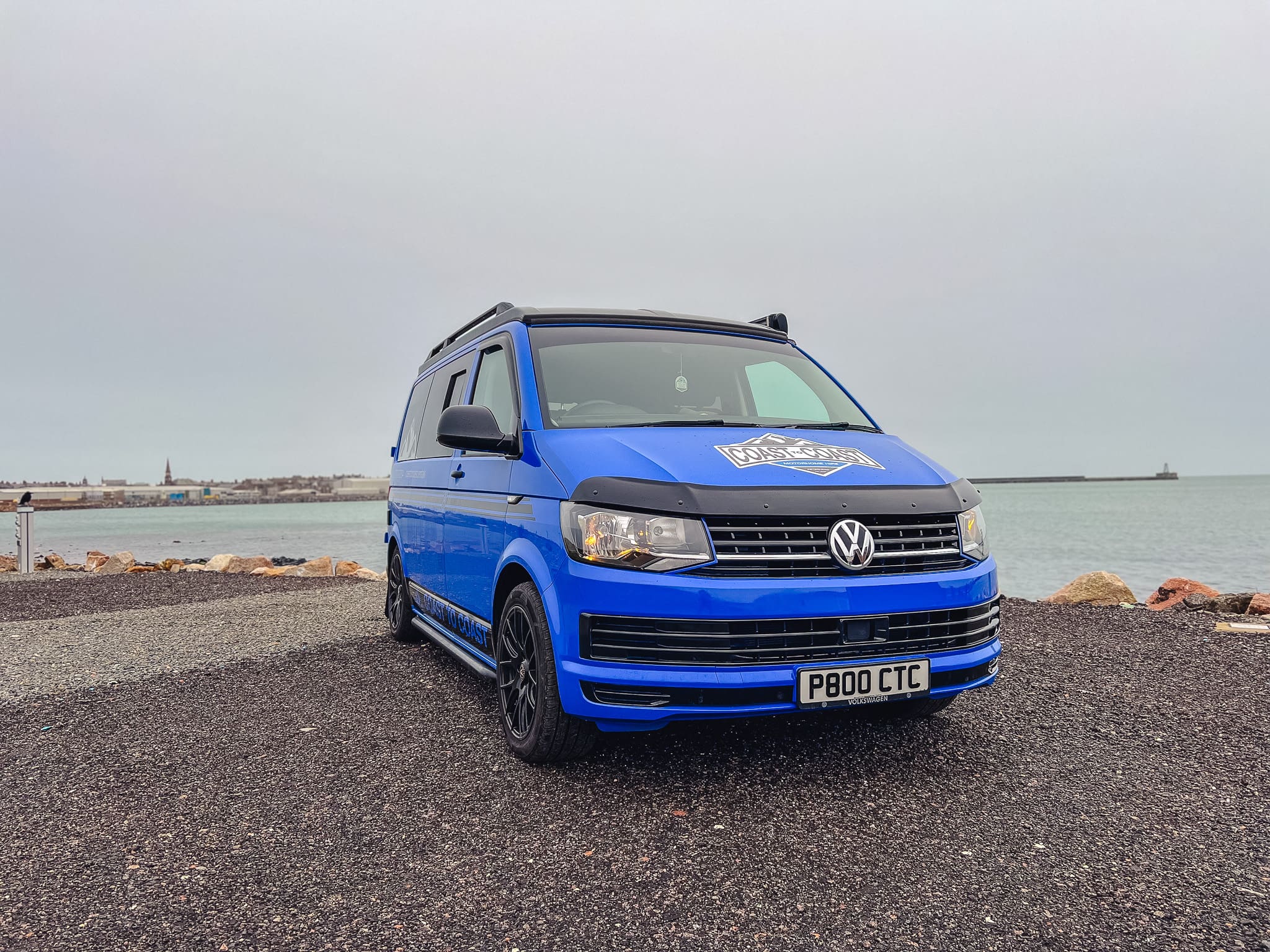 Blue VW T6 Coast to Coast campervan with branding, parked by the coast near Peterhead, Scotland – available for campervan hire