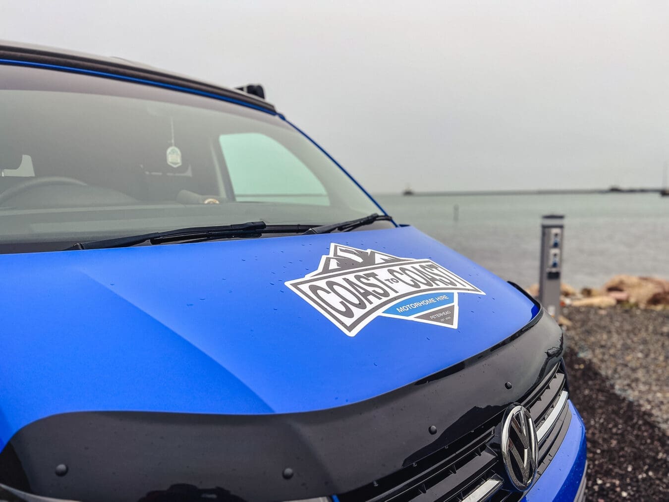Home 21 Close-up of Coast to Coast campervan hire logo on blue VW van parked by the sea in Peterhead, Scotland