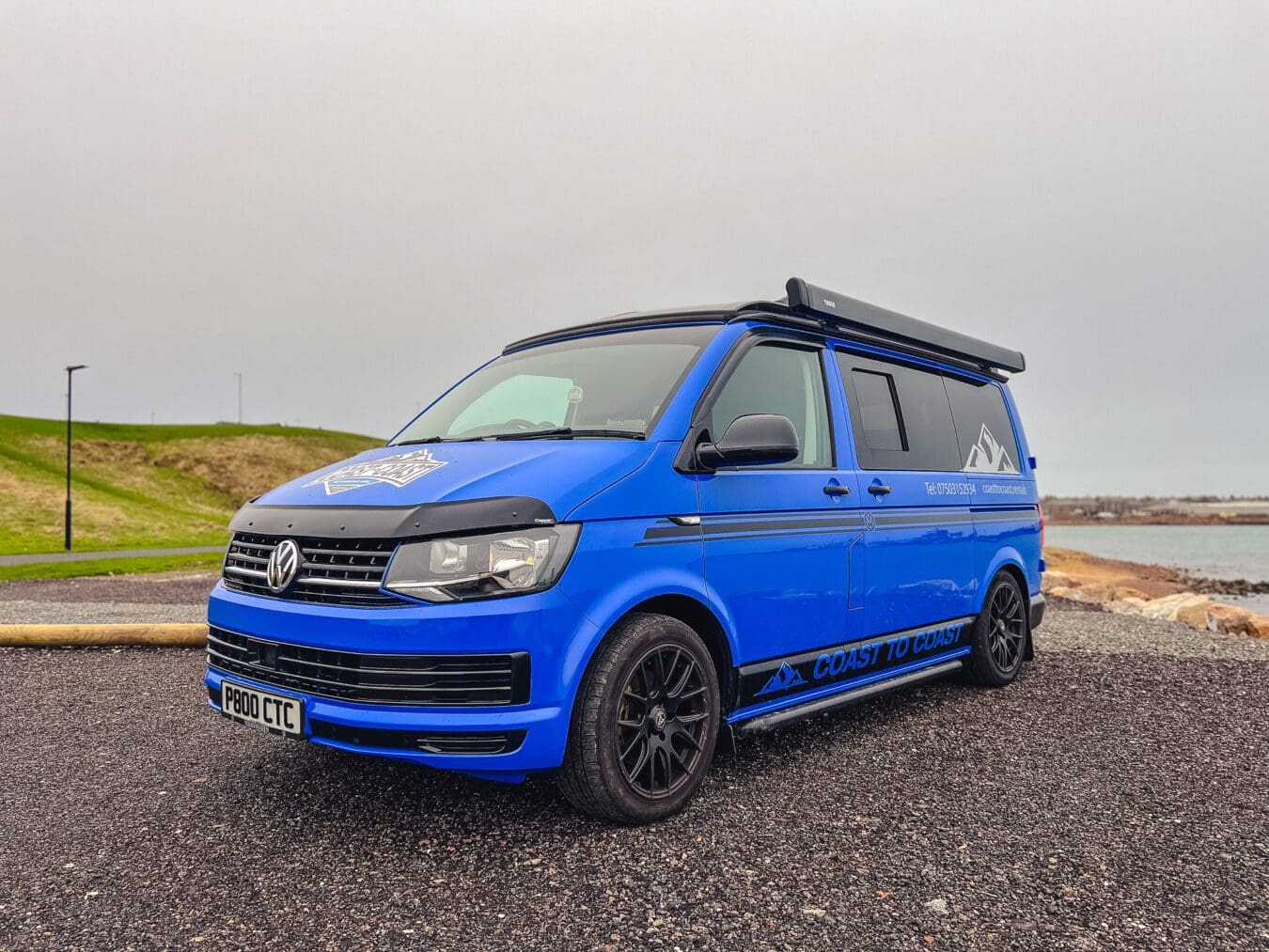 Home 20 Blue VW T6 Coast to Coast campervan with branding, parked by the coast near Peterhead, Scotland – available for campervan hire