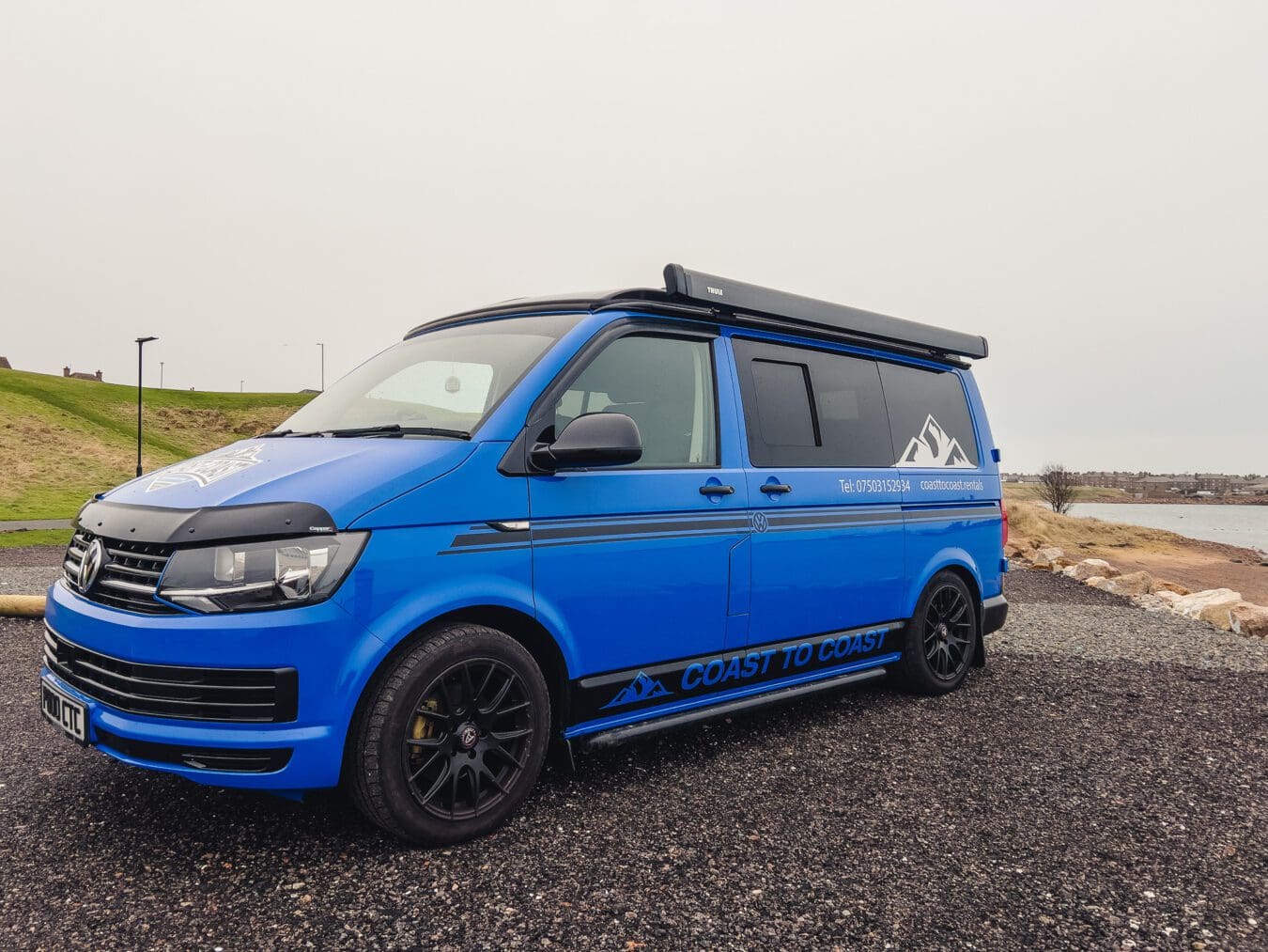 Home 26 Blue VW T6 Coast to Coast campervan with branding, parked by the coast near Peterhead, Scotland – available for campervan hire