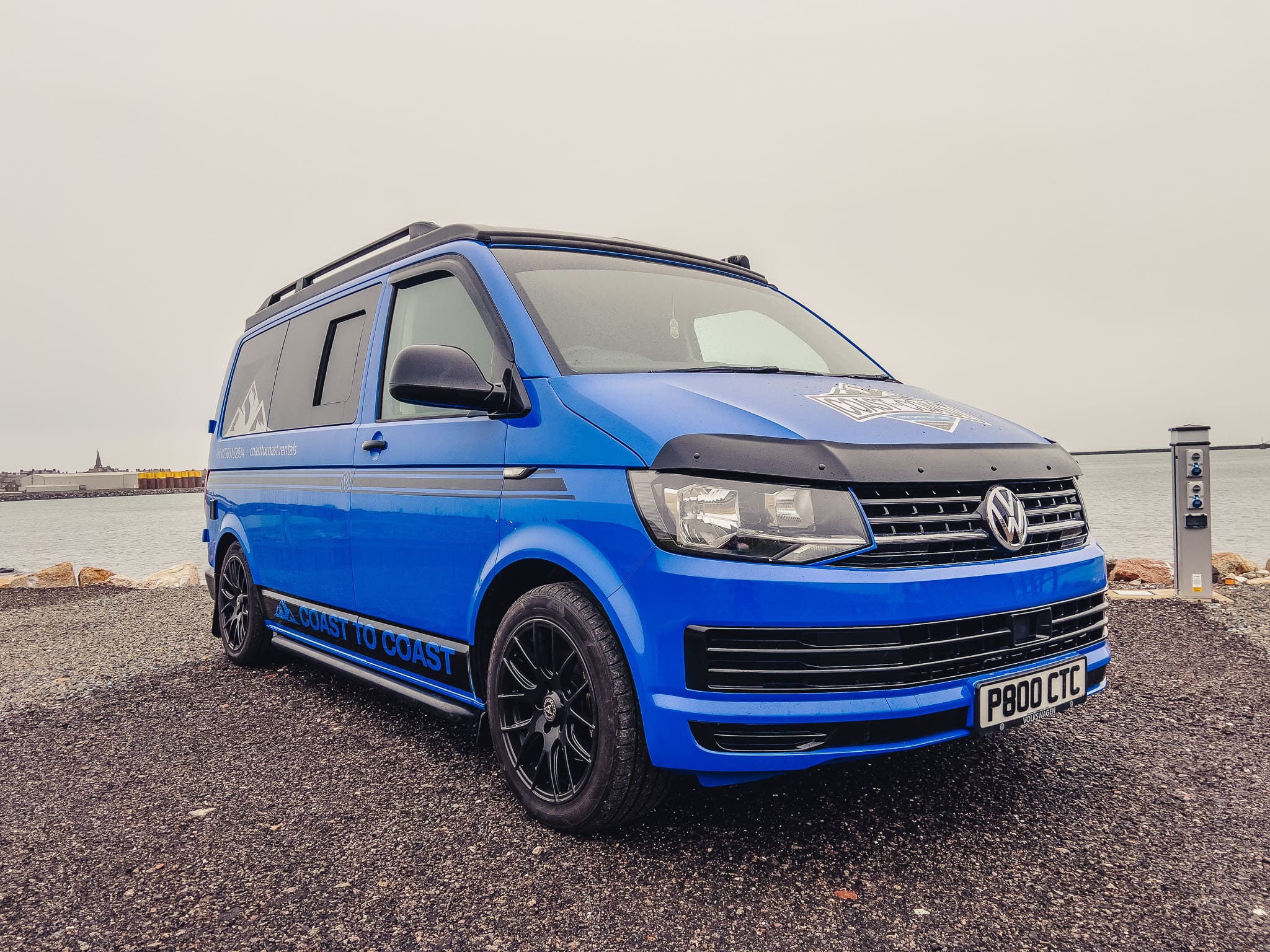 Blue VW T6 Coast to Coast campervan with branding, parked by the coast near Peterhead, Scotland – available for campervan hire
